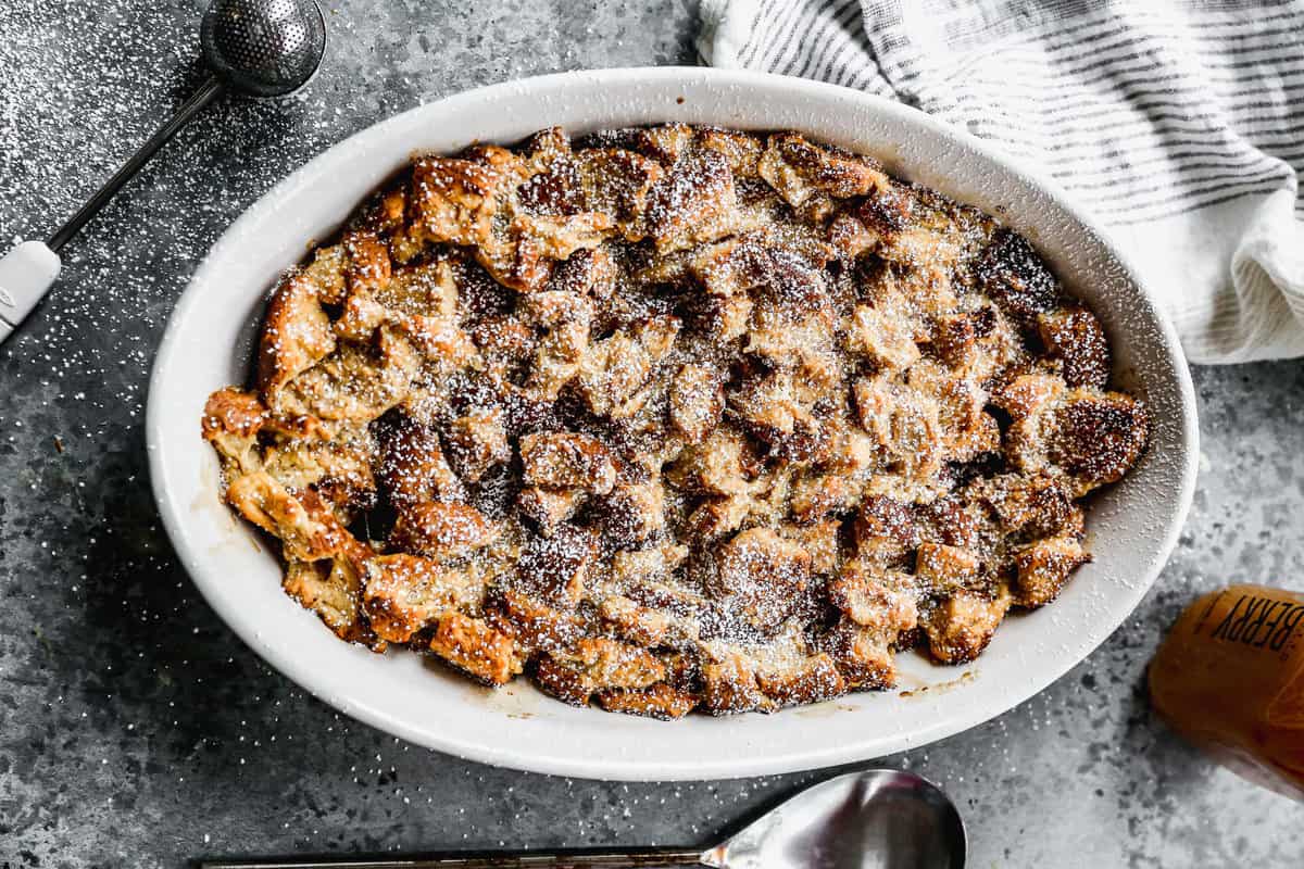 An oval baking dish with baked bread pudding, dusted with powdered sugar.