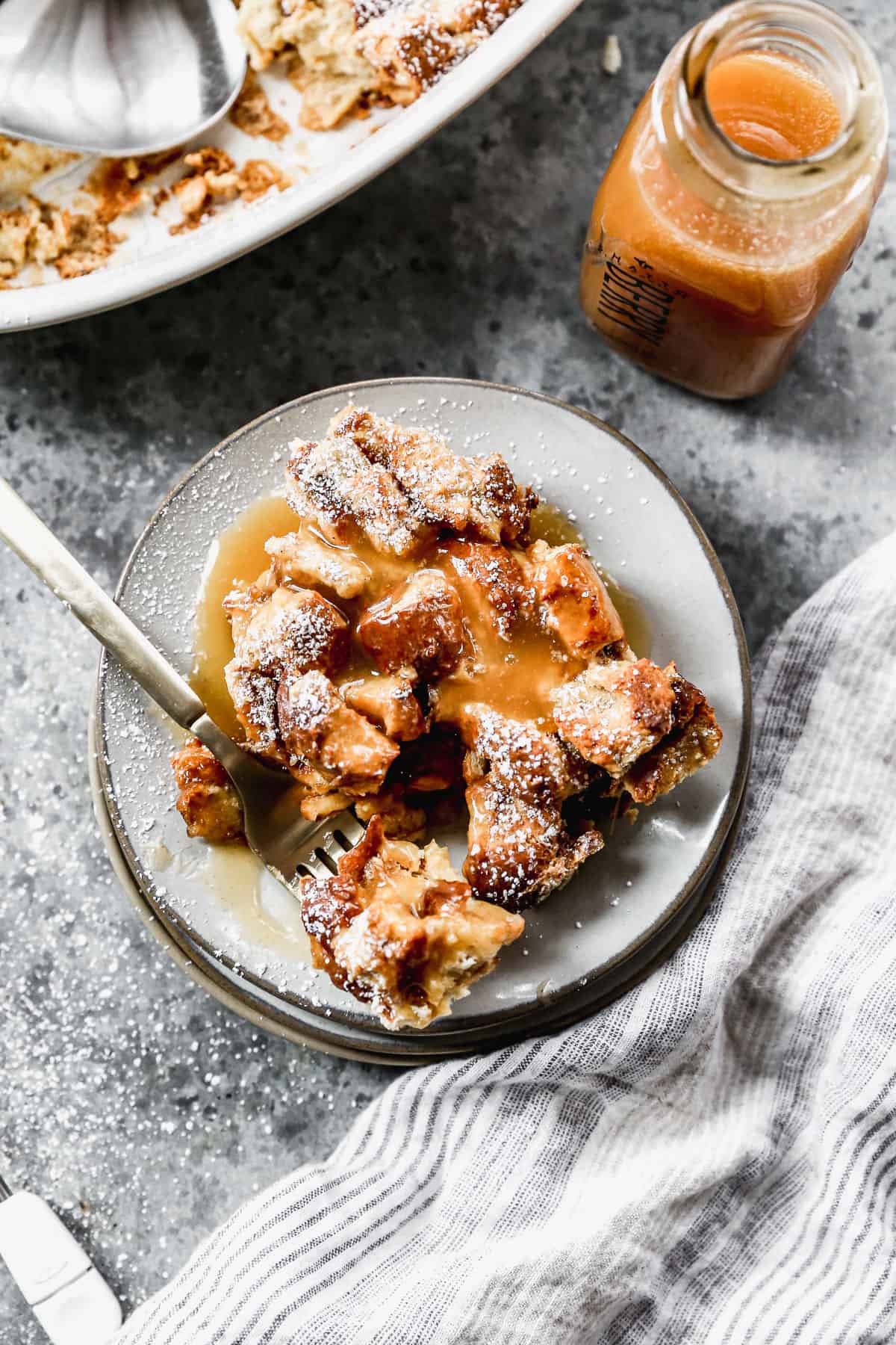 A piece of easy Bread Pudding on a plate with powdered sugar dusted on top and drizzled with caramel sauce.