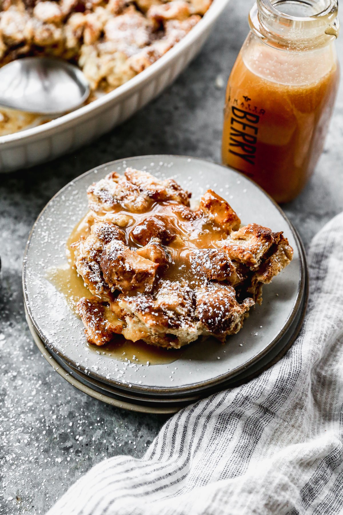 A piece of Bread Pudding on a plate dusted with powdered sugar and drizzled with caramel sauce, ready to enjoy. 