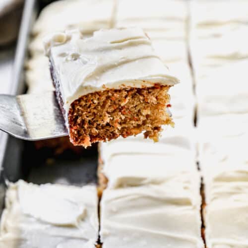 A piece of easy carrot cake with whipped cream cheese frosting being lifted from a 9x13 baking pan to serve.
