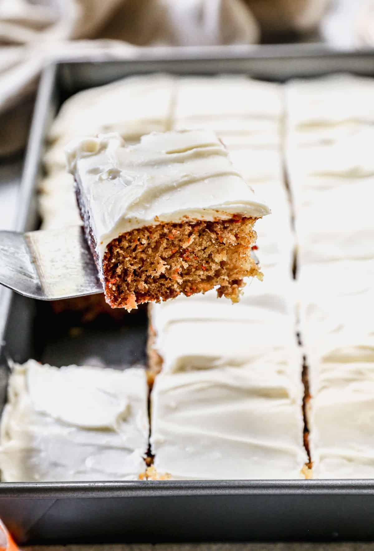 A piece of easy carrot cake being lifted from a 9x13 baking dish with a small spatula.