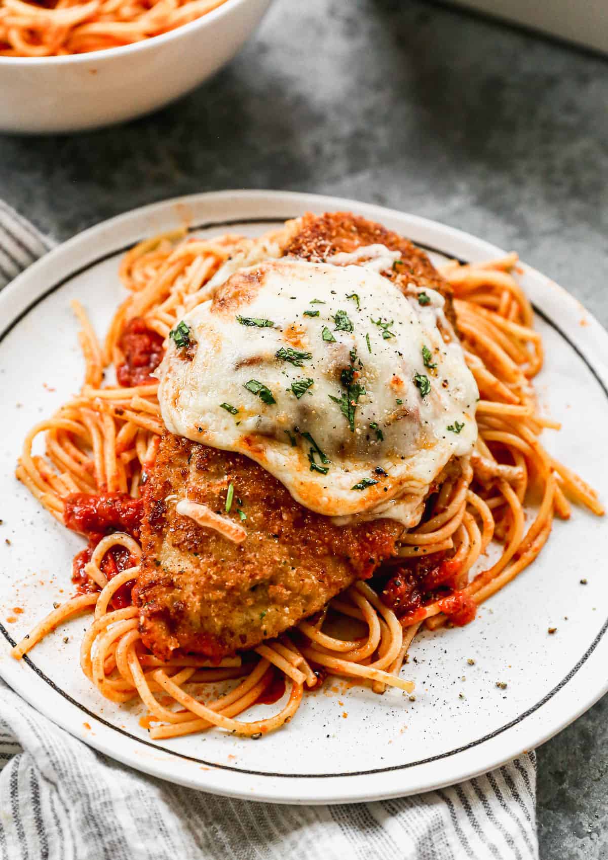 Chicken Parmesan with melted cheese, sitting on top of a pile of pasta.