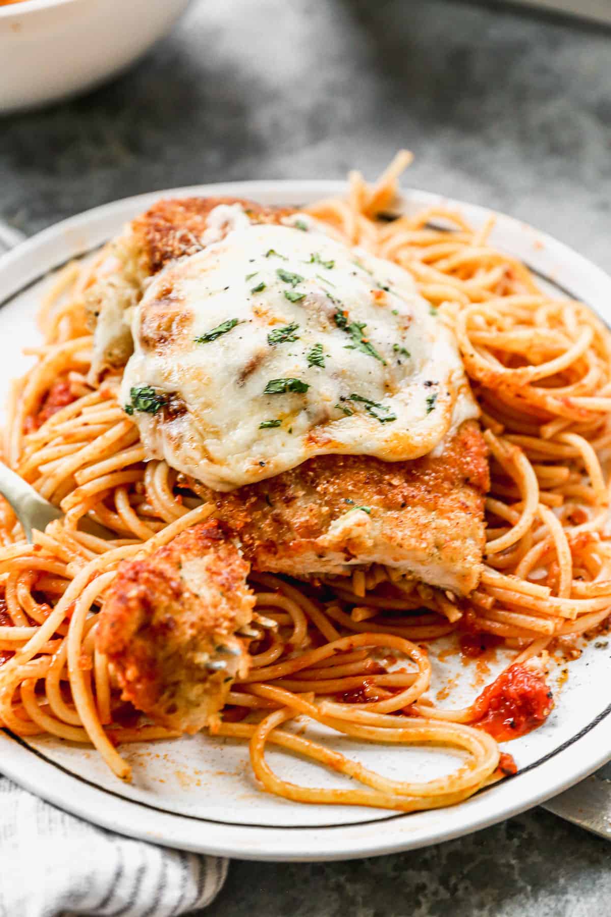A close up image of homemade Chicken Parmesan, with a fork scooping up a bite.