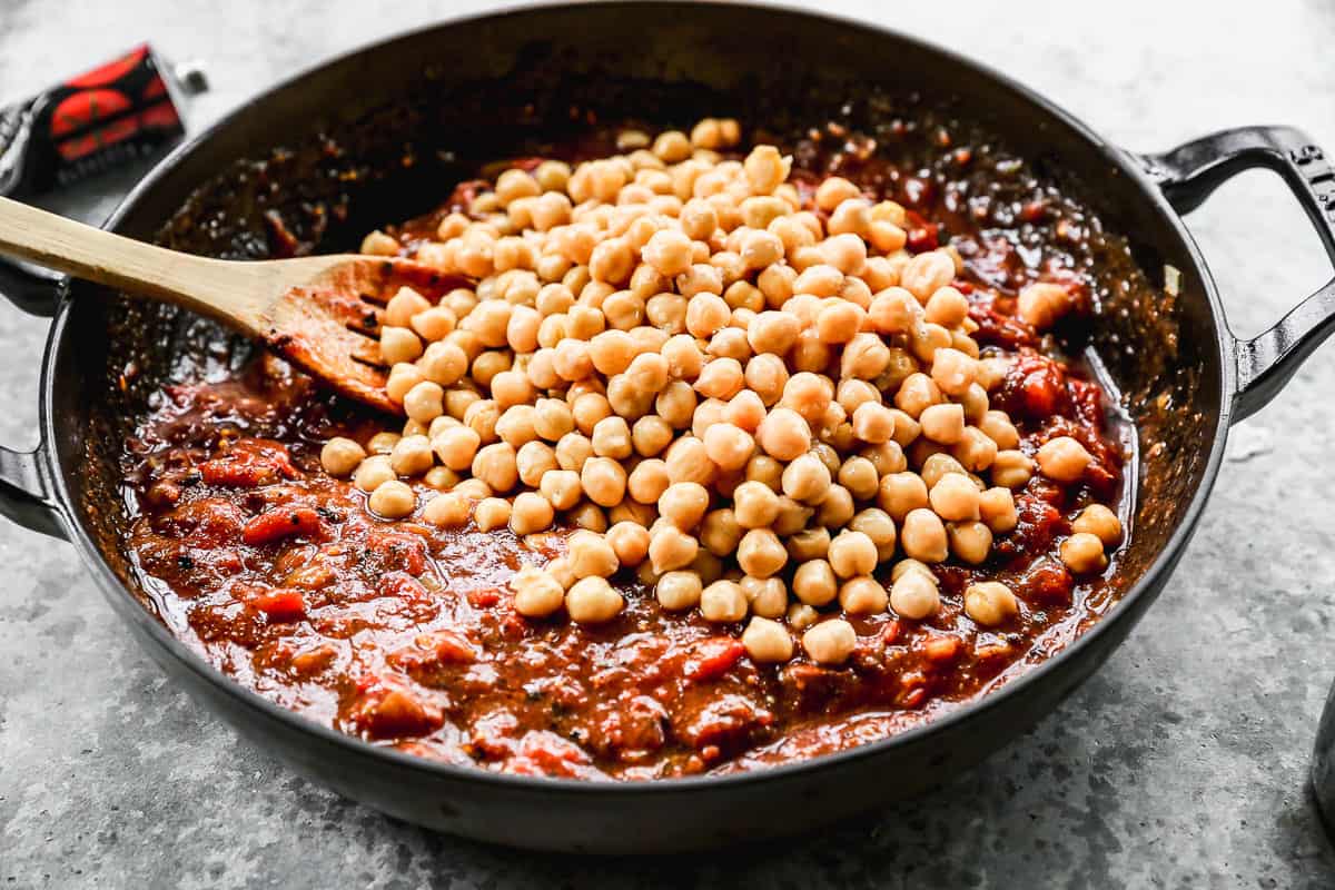 Chickpeas being added to a curry sauce in a large pan.