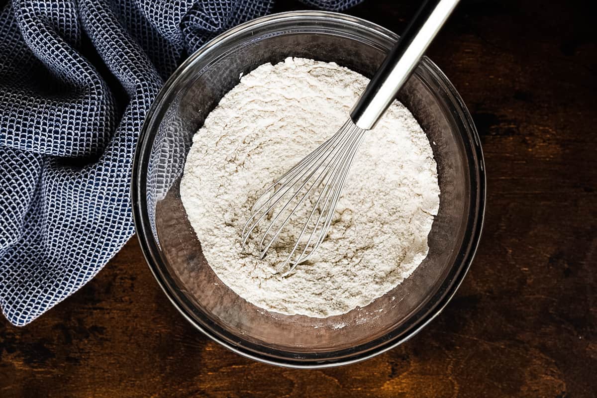 A glass bowl filled with flour, baking powder, and salt.