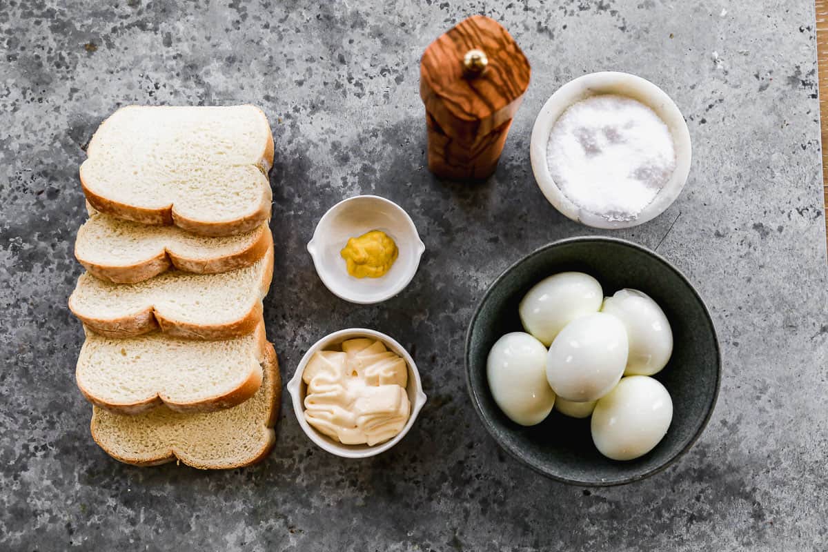 All the ingredients needed to make the best egg salad sandwich: bread, mayo, mustard, boiled eggs, and salt and pepper.