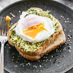 A poached egg with the yolk slightly exposed on top of a piece of avocado toast.