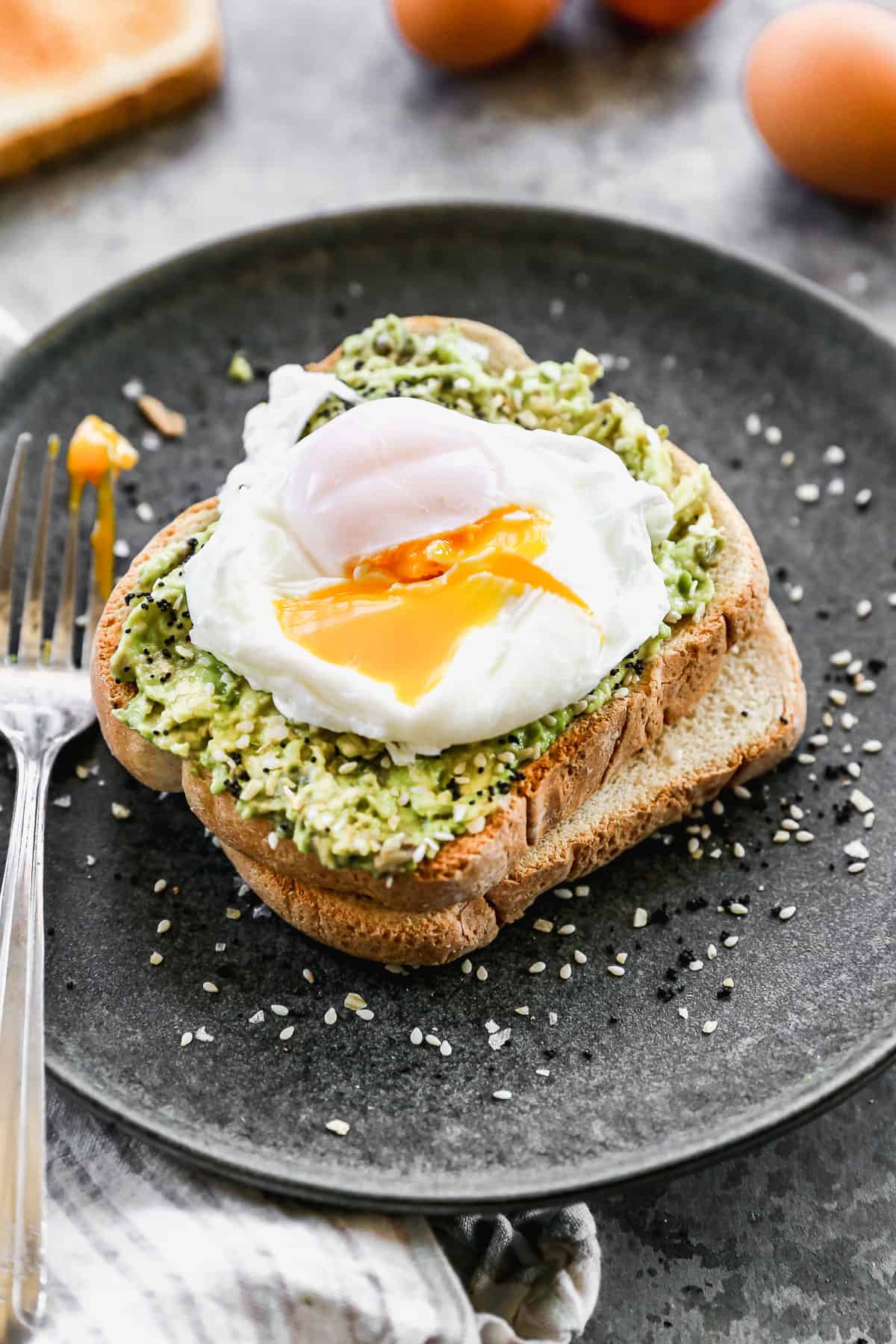 A poached egg slightly cut to reveal the yolk on top of a slice of avocado toast.