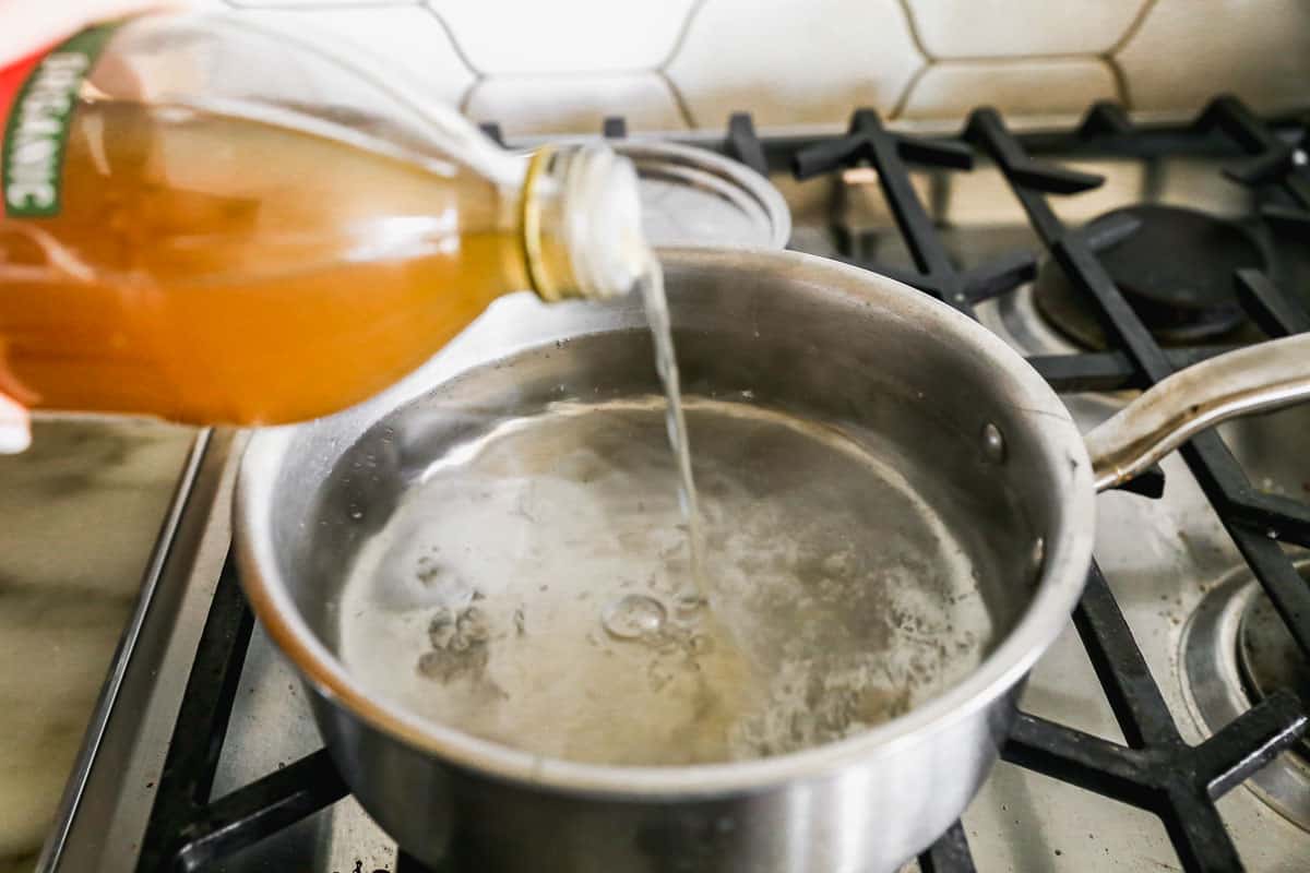 Apple cider vinegar being poured into a pot of simmering water for the best poached egg recipe.