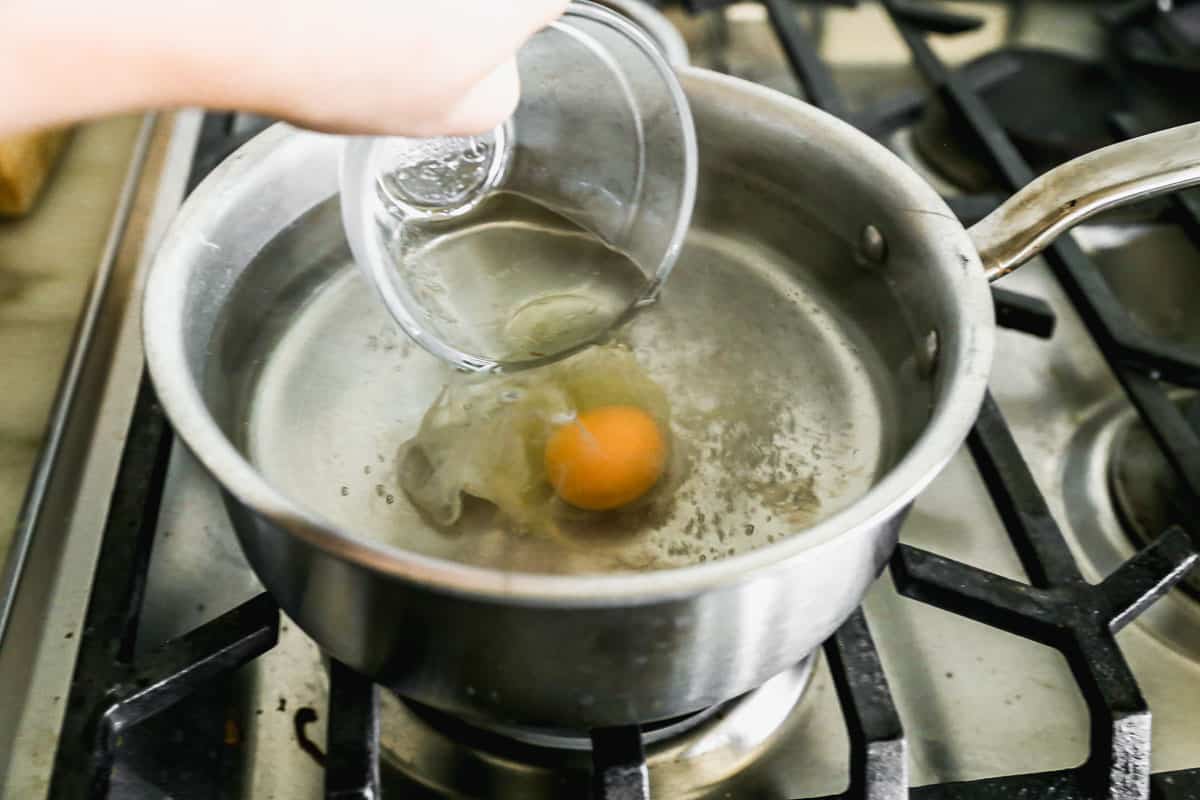 An egg being poured into a pot of simmering water to make a poached egg.