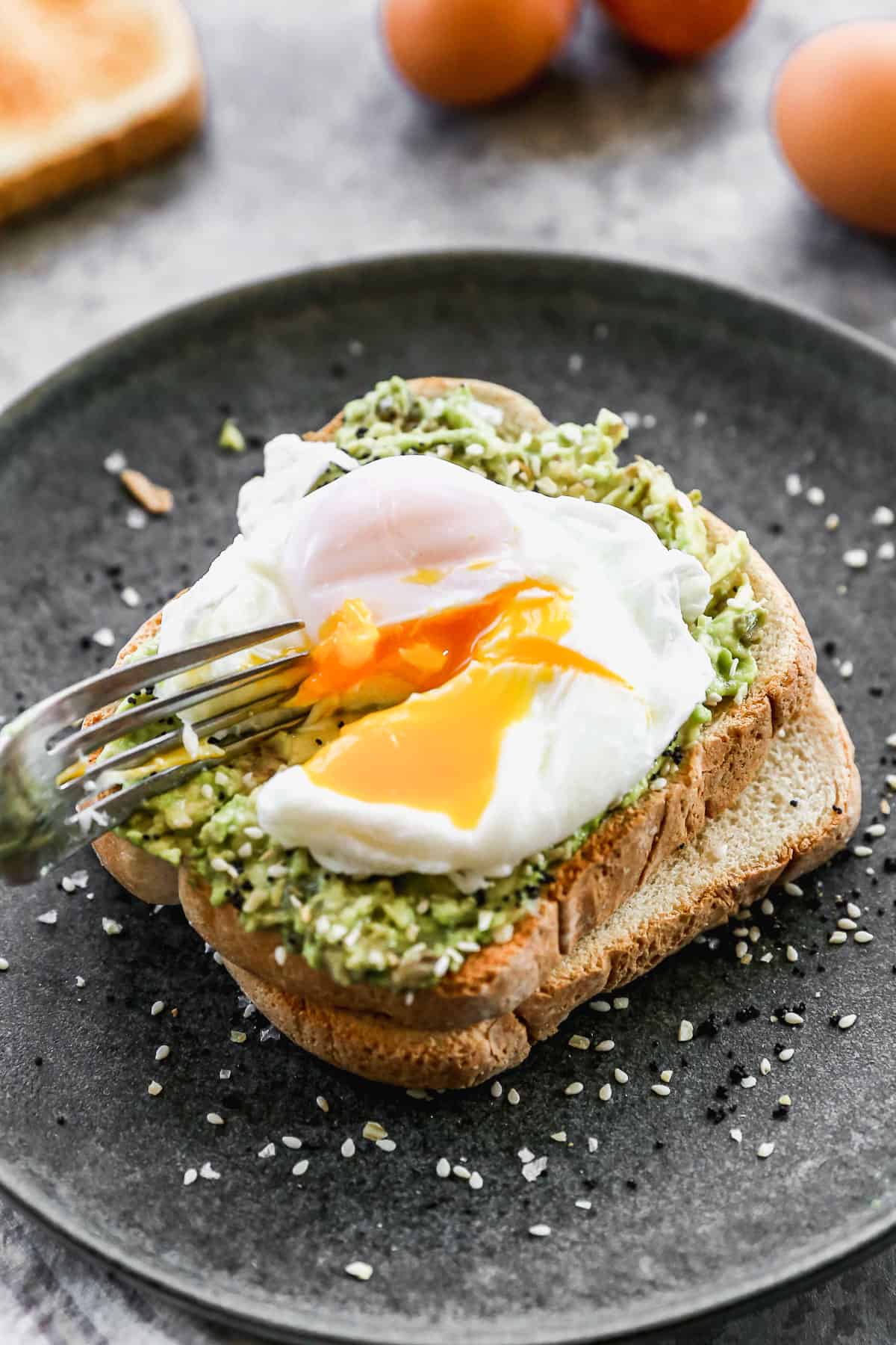 A fork cutting a poached egg on the top of avocado toast. 