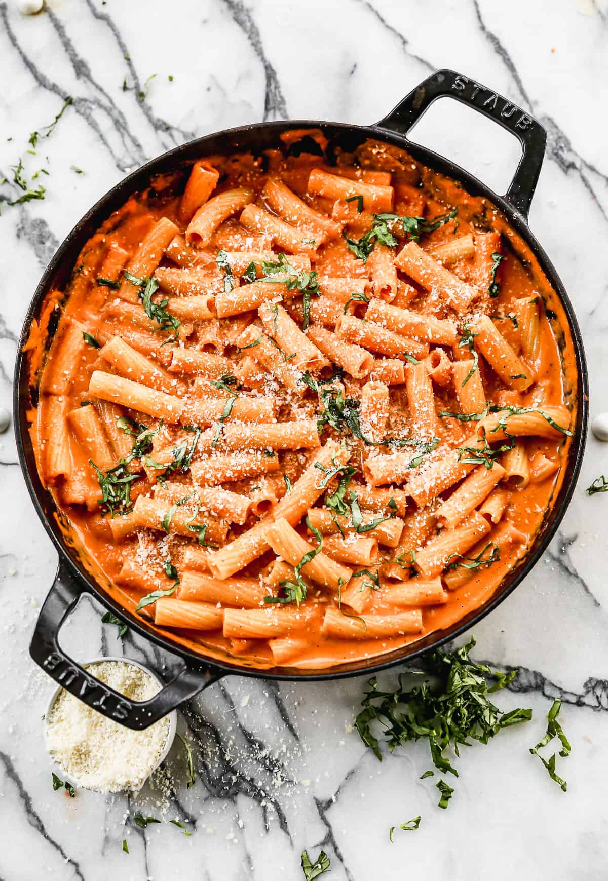 Pink sauce pasta with rigatoni pasta served in a skillet, garnished with fresh basil and parmesan.