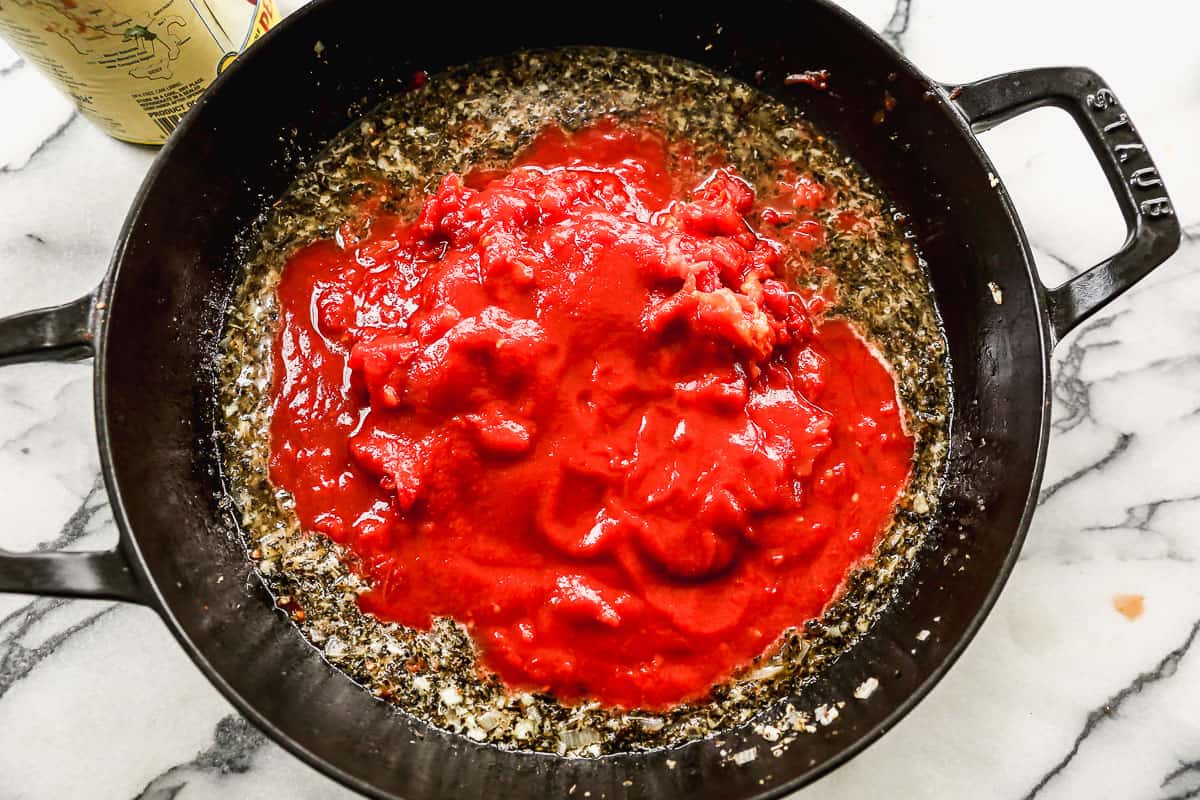 Whole peeled tomatoes, spices and diced shallot in a saucepan to make pink sauce pasta.