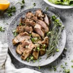 A plate with the best pork tenderloin recipe, sliced on a plate and garnished with fresh herbs.