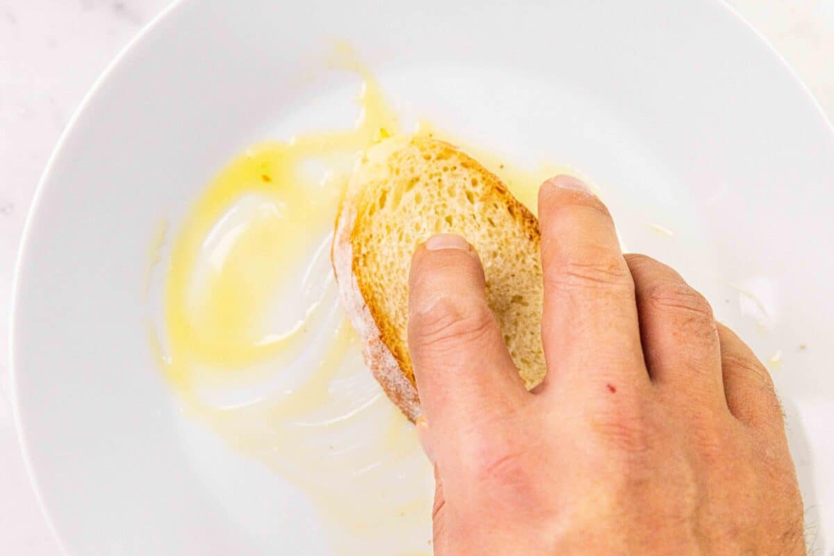 A slice of bread being dipping into a plate with some olive oil on it.