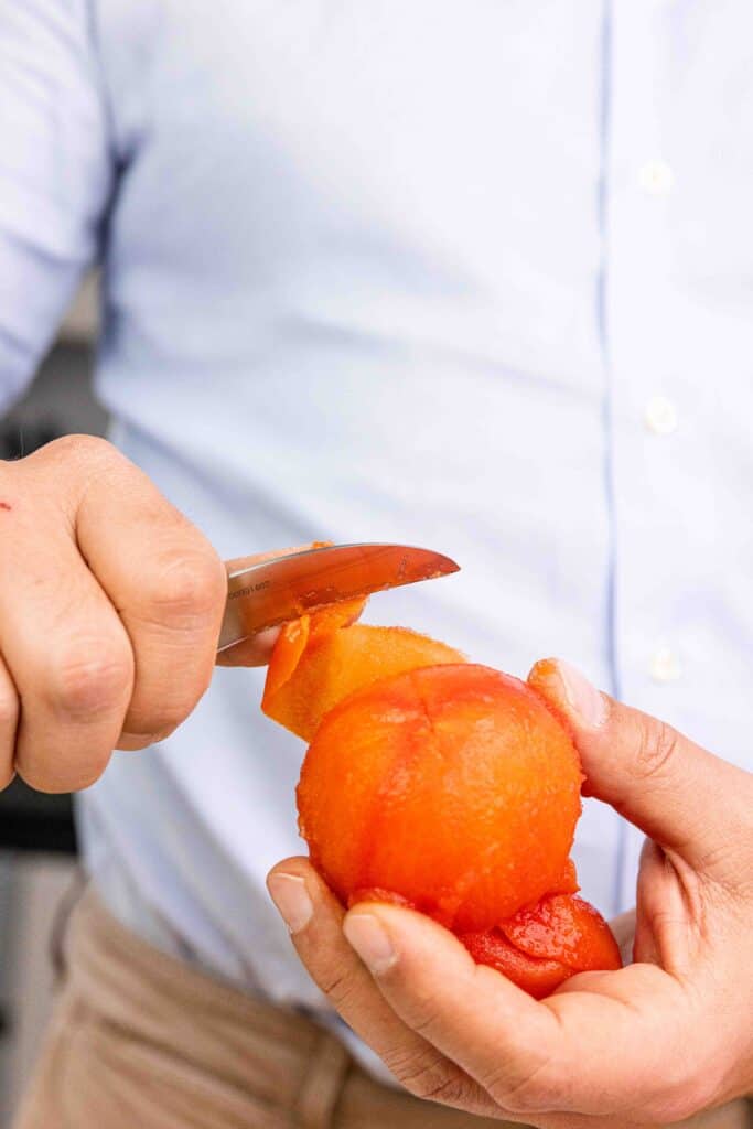 A small knife peeling the skin off a tomato.