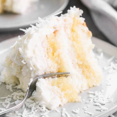 A slice of an easy coconut cake recipe with a pineapple filling on a plate with a fork cutting into it.