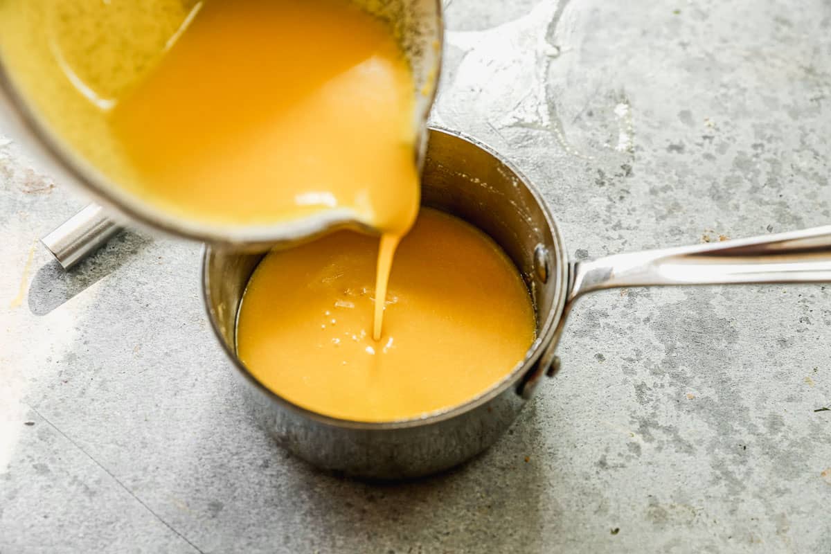 An easy hollandaise sauce being poured back into a saucepan to keep warm for Crab Cake Benedict.
