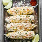 Four ears of Elote, or Mexican Street Corn on a baking sheet, ready to serve.