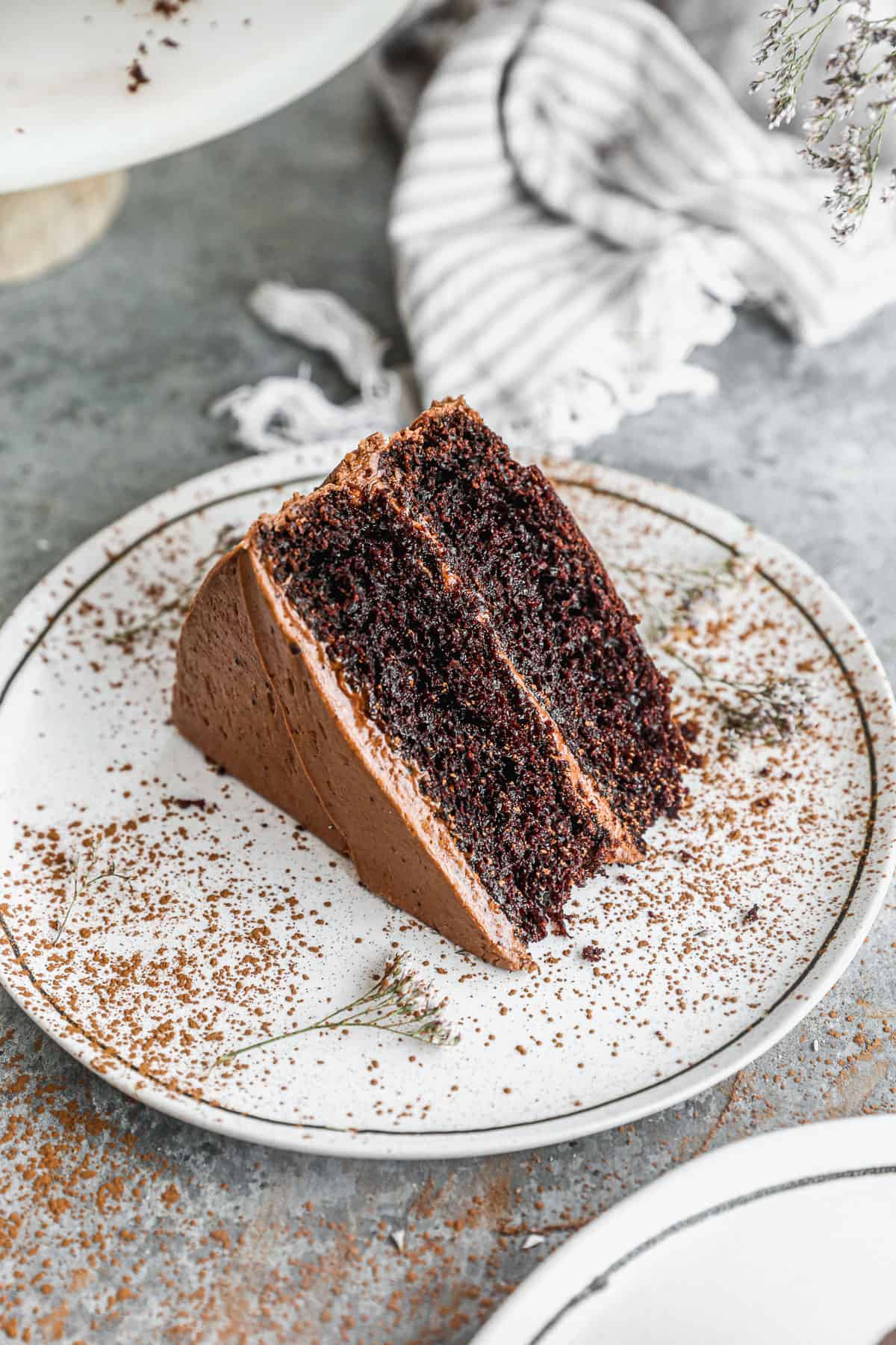 A slice of a two layer chocolate cake on a white plate, dusted with cocoa powder.