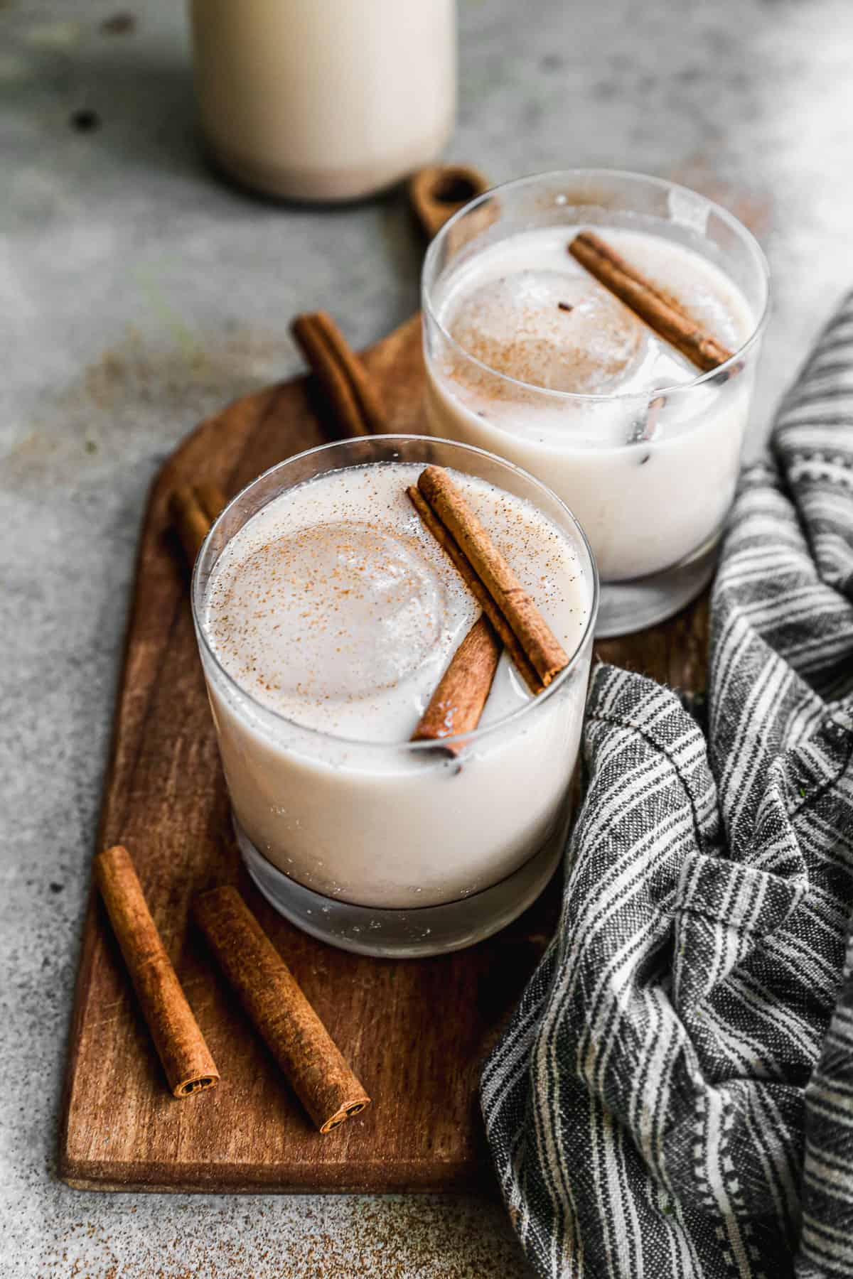 Two glasses of Horchata in a glass with ice and topped with two cinnamon sticks and a sprinkle of cinnamon.
