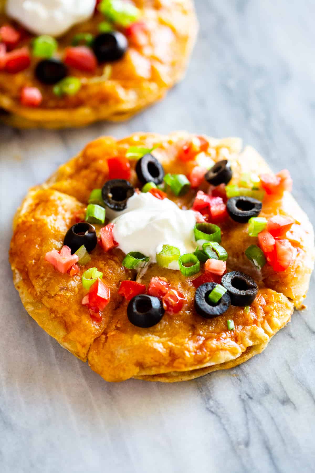 A homemade Mexican Pizza topped with olives, tomatoes, green onions, and sour cream.