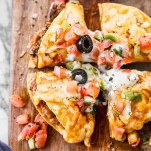 The best Taco Bell Mexican Pizza recipe served on a wooden cutting board, cut into fourths and topped with olives, chopped tomatoes, green onions, and sour cream.