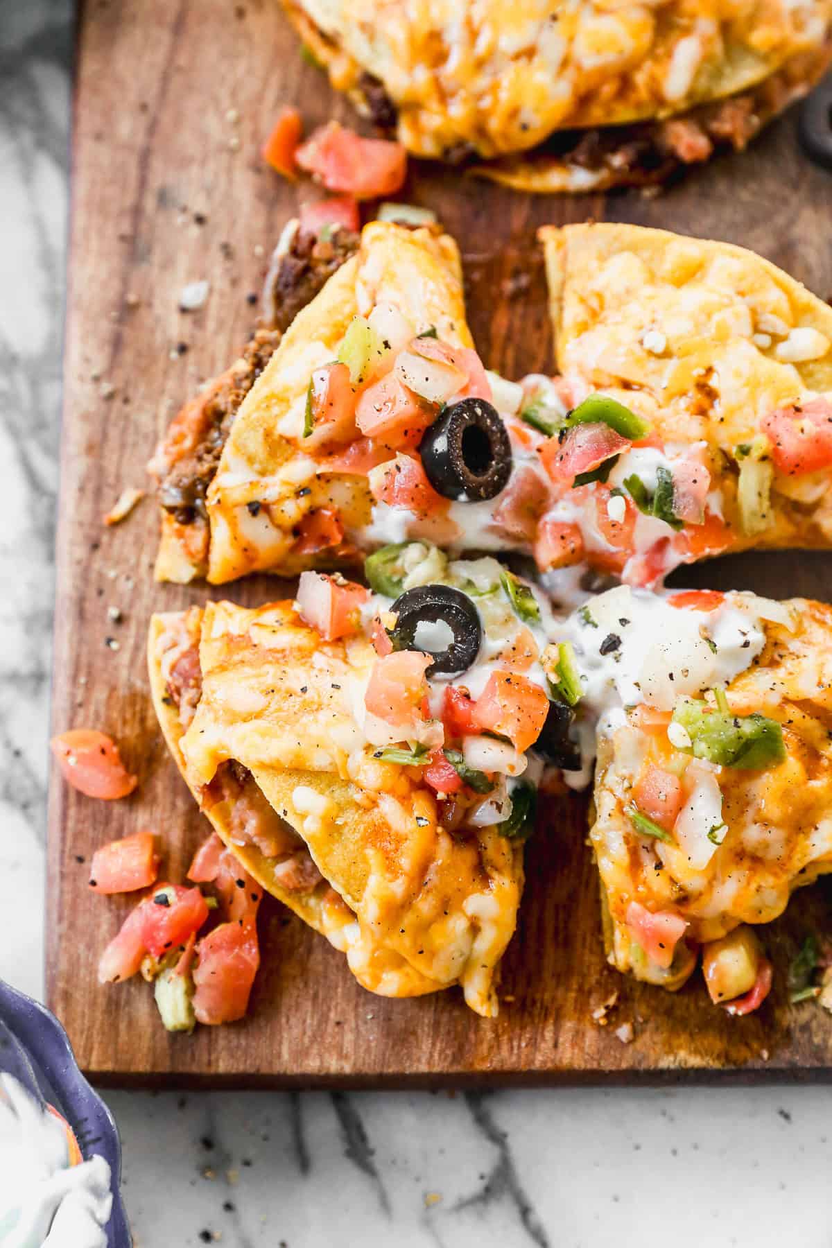 The best Taco Bell Mexican Pizza recipe served on a wooden cutting board, cut into fourths and topped with olives, chopped tomatoes, green onions, and sour cream.
