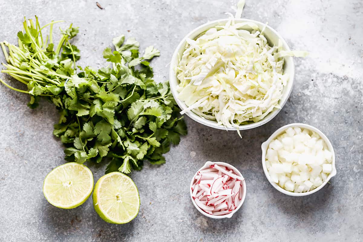 Pozole toppings prepped and ready including: cilantro, lime, shredded cabbage, sliced radishes, and diced onion.