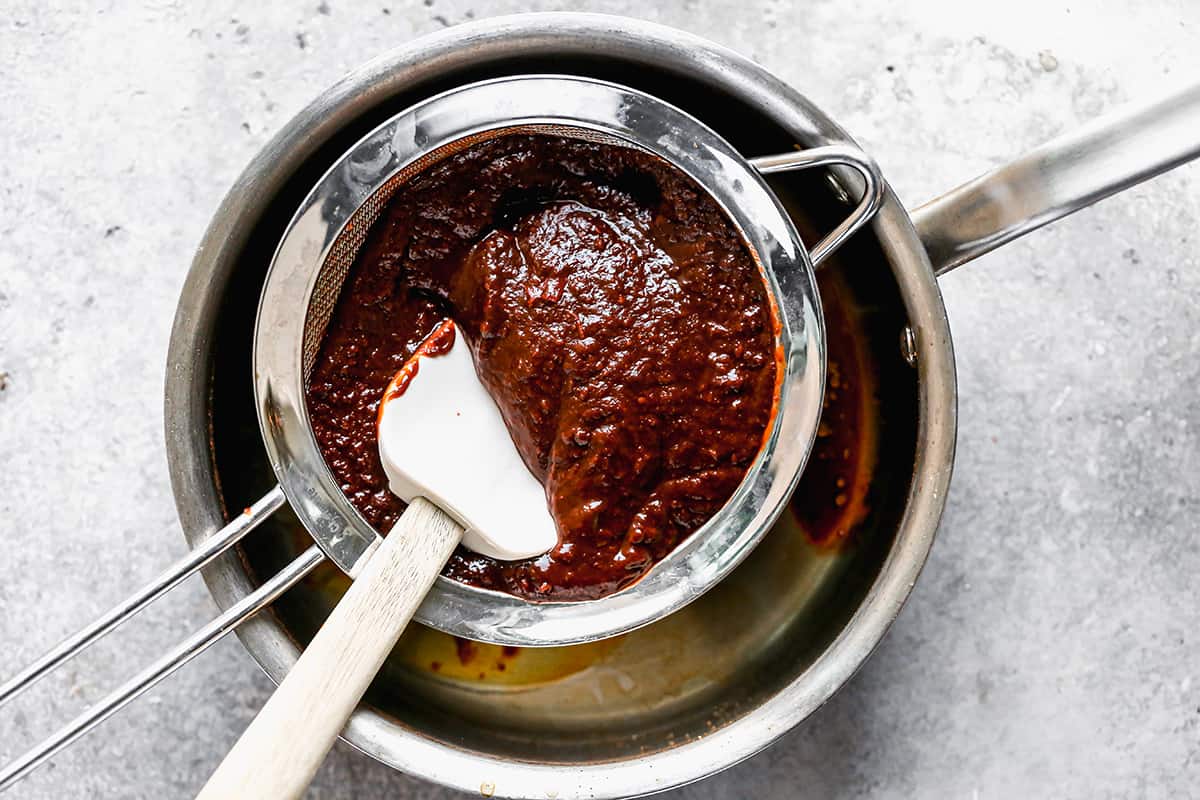 Blended red chile sauce being pushed through a fine mesh strainer into a pot.