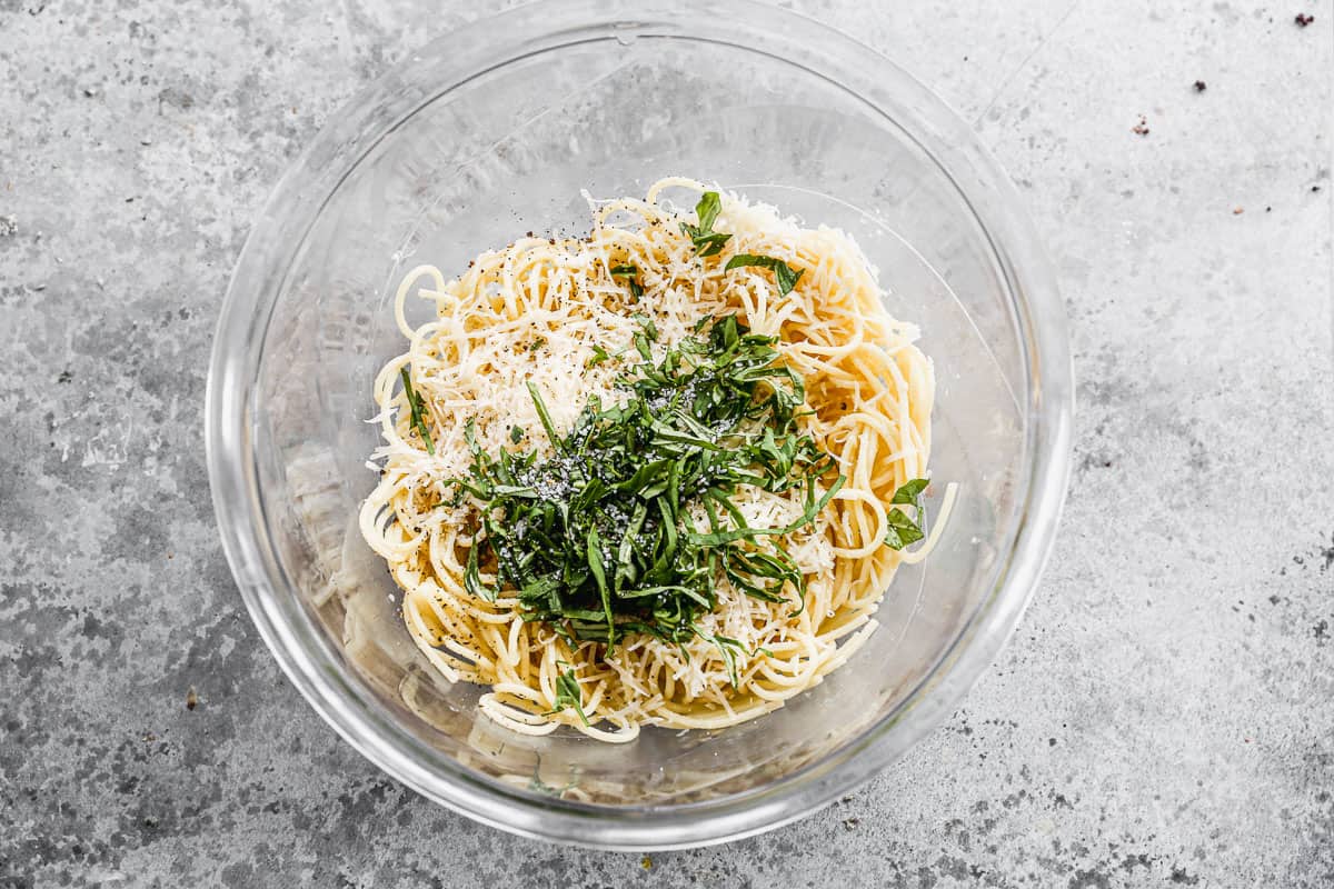 Spaghetti noodles in a glass bowl with egg, parmesan cheese, butter, and basil to make easy Spaghetti PIe.