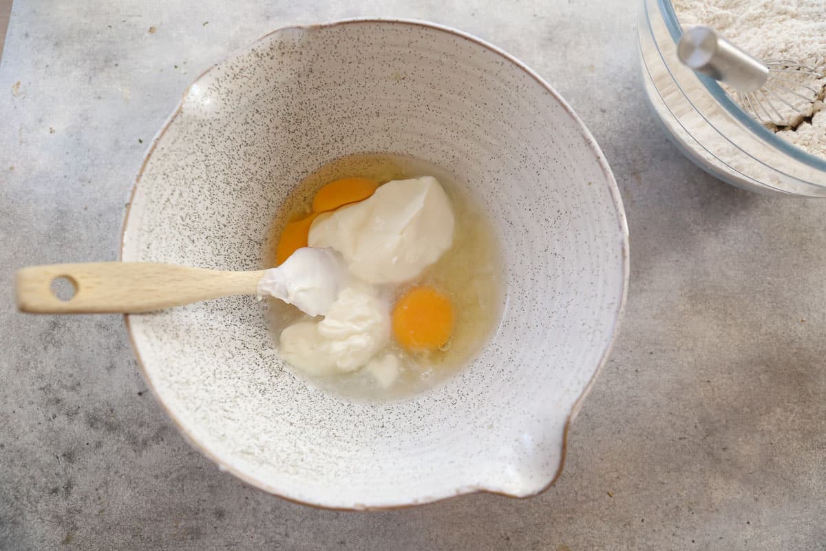 Sour cream, eggs, and vanilla in a white mixing bowl.