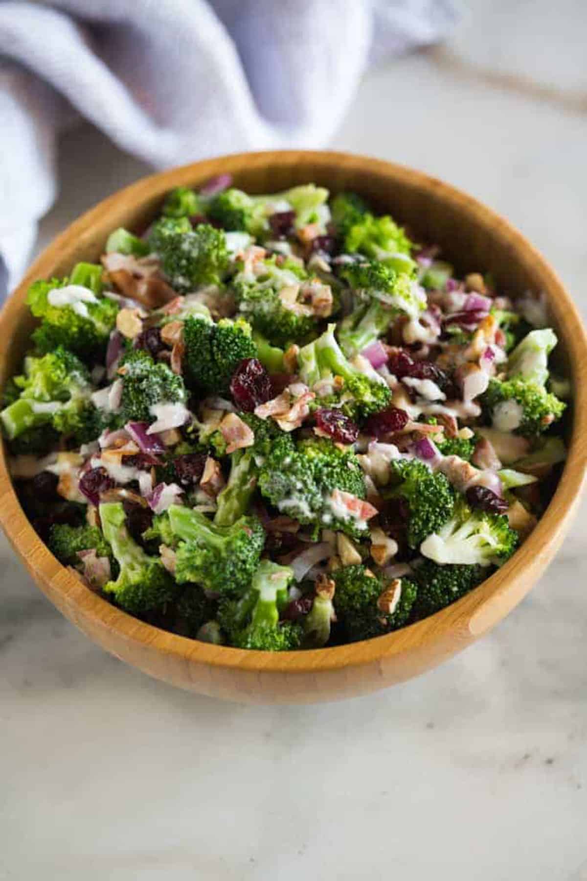Broccoli Salad in a large wooden bowl with pieces of bacon, craisins, and a delicious dressing.