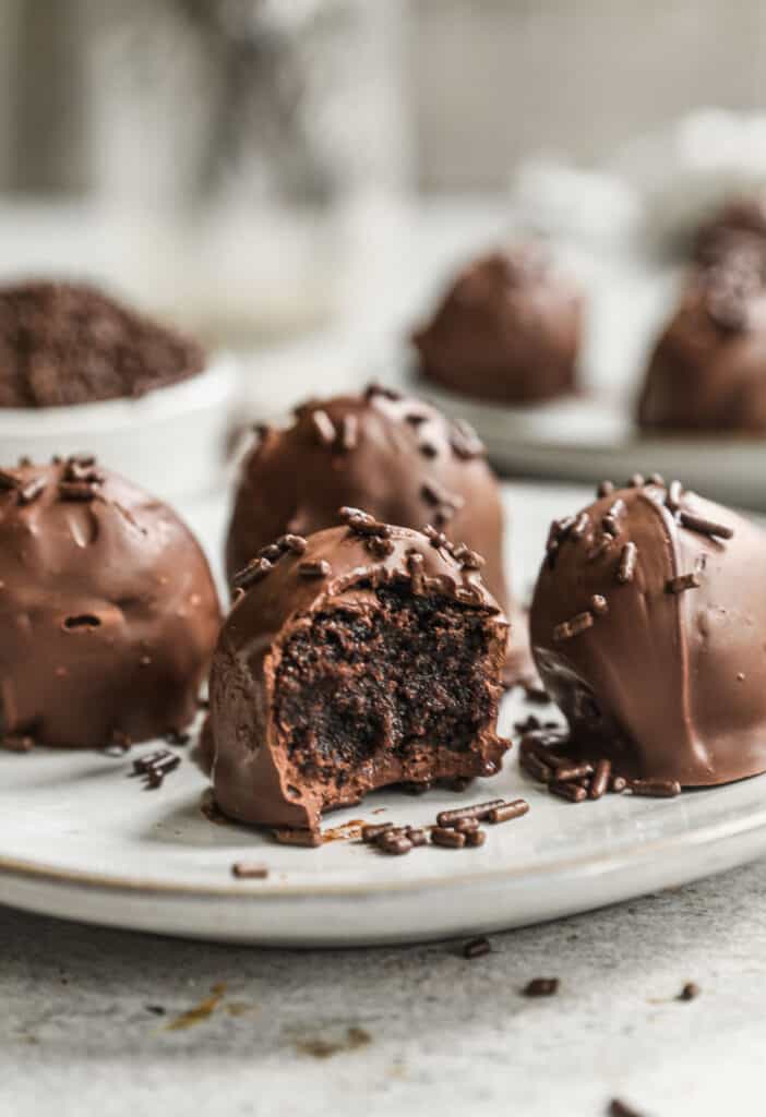 Four homemade brownie truffles on a plate, the one in the front is bitten in half.
