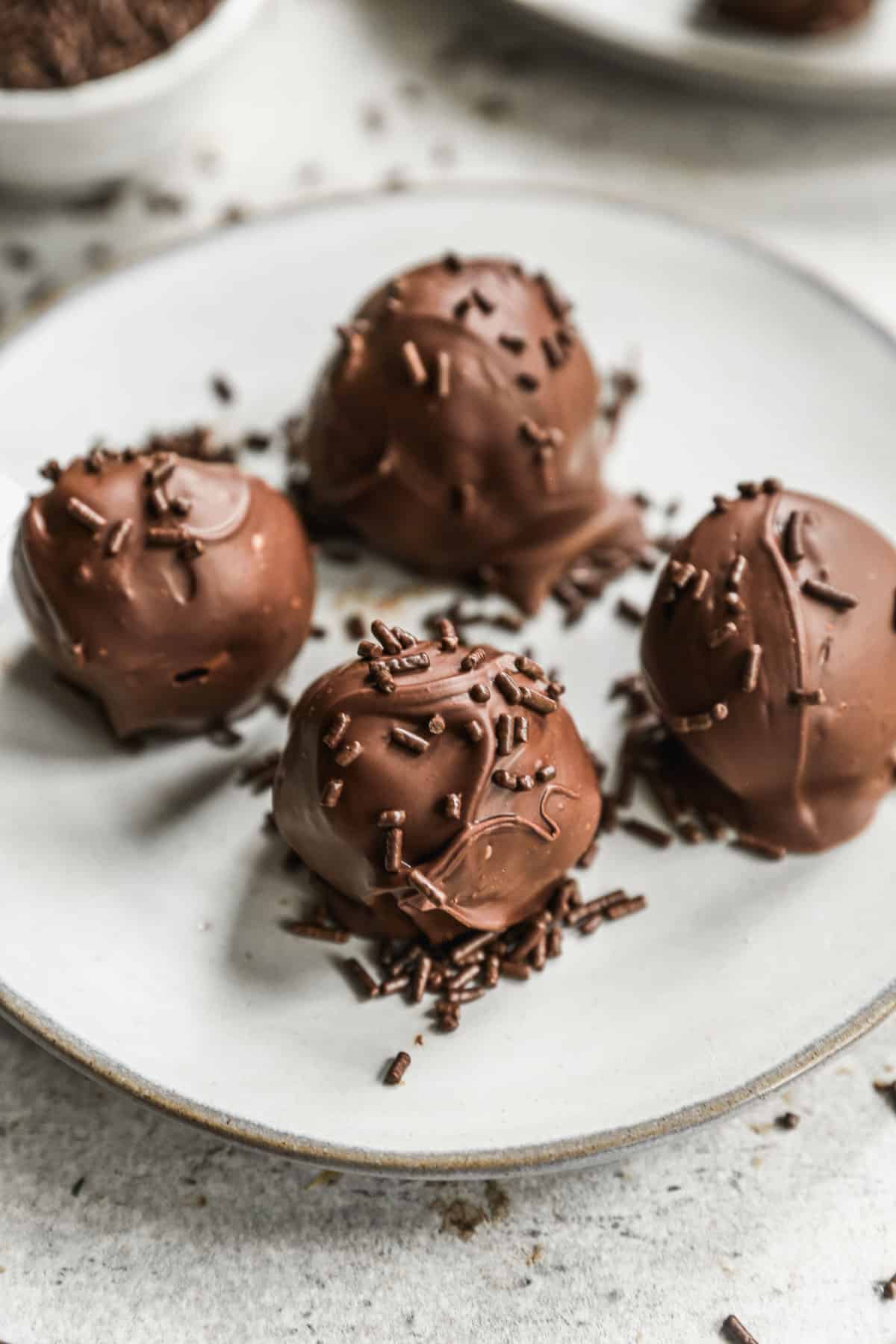 Four easy brownie balls on a white plate topped with chocolate sprinkles.