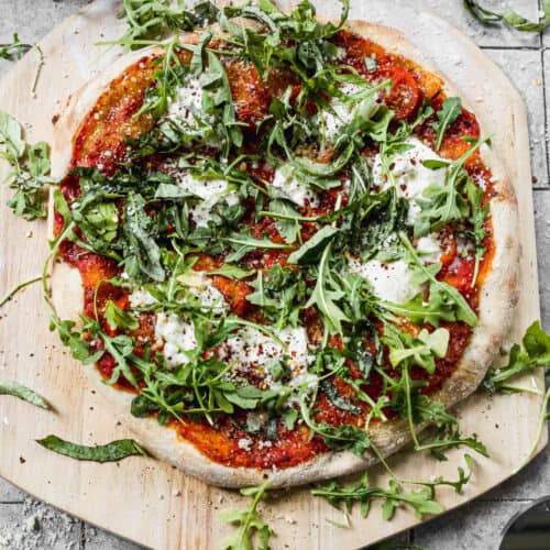 An easy Burrata Pizza topped with fresh arugula and a drizzle of balsamic reduction, on a wooden pizza peel.