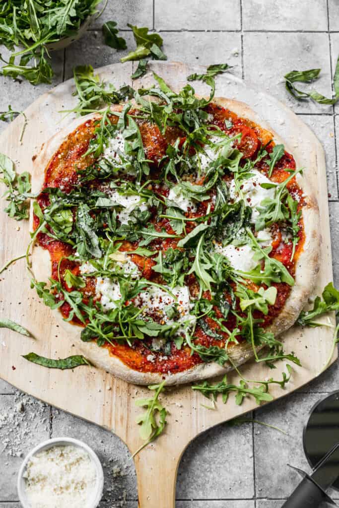 An easy Burrata Pizza topped with fresh arugula and a drizzle of balsamic reduction, on a wooden pizza peel.