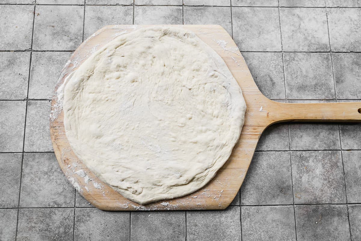 Homemade pizza dough stretched into a circle on a floured pizza peel.