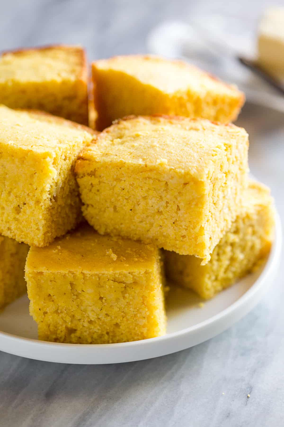 Squares of Buttermilk Cornbread stacked on a white plate.