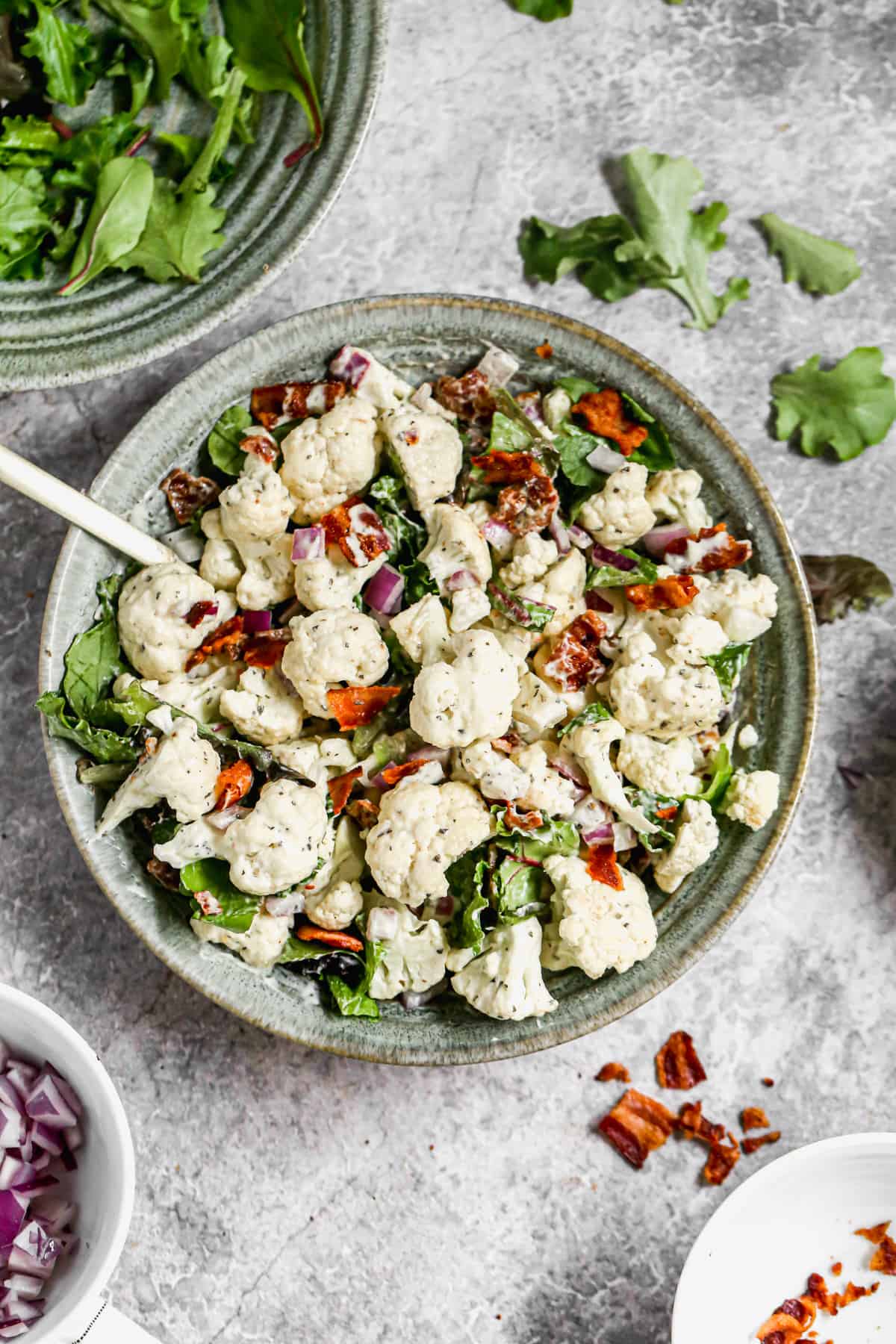 A bowl of cauliflower salad with crispy bacon bits in a large bowl.