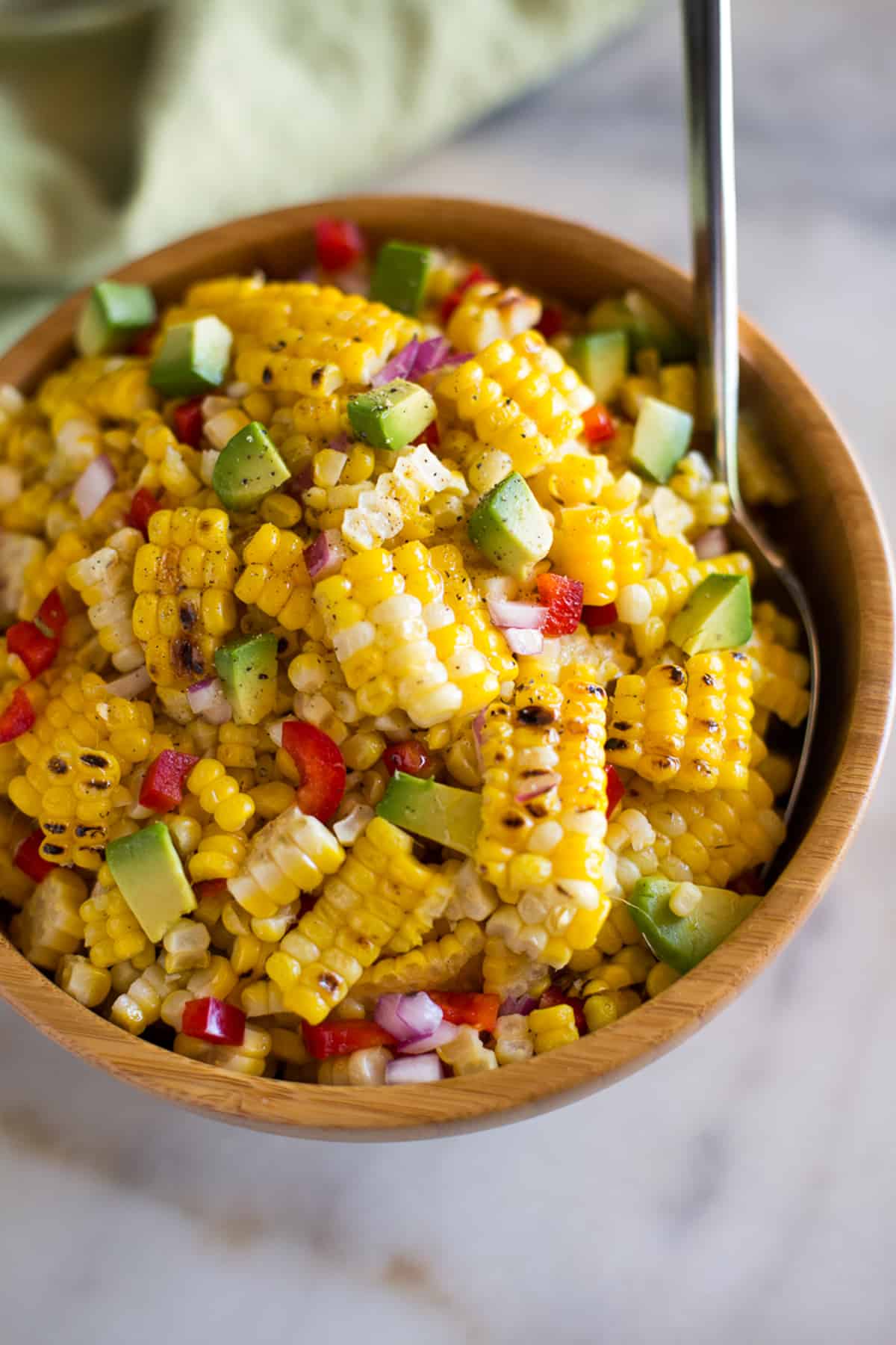 A fresh corn salad in a wooden bowl with bell pepper, red onion, and avocado.