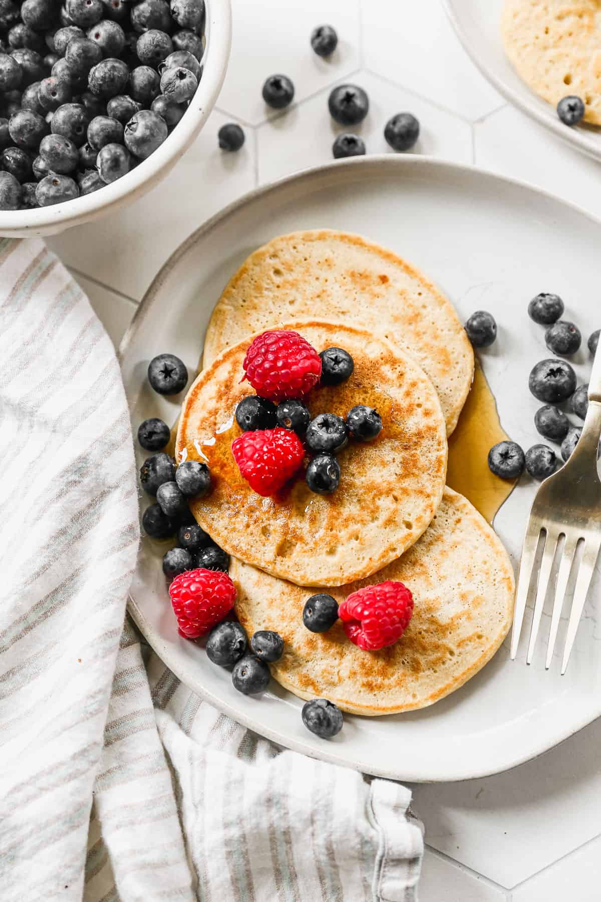 Three easy Cottage Cheese Pancakes on a plate with blueberries and raspberries, drizzled with maple syrup.
