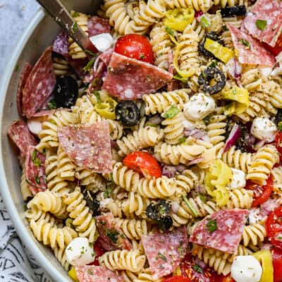 A zesty Italian Pasta Salad recipe served in a large bowl with rotini pasta, mozzarella cheese pearls, salami, black olives, cherry tomatoes, and parmesan cheese.