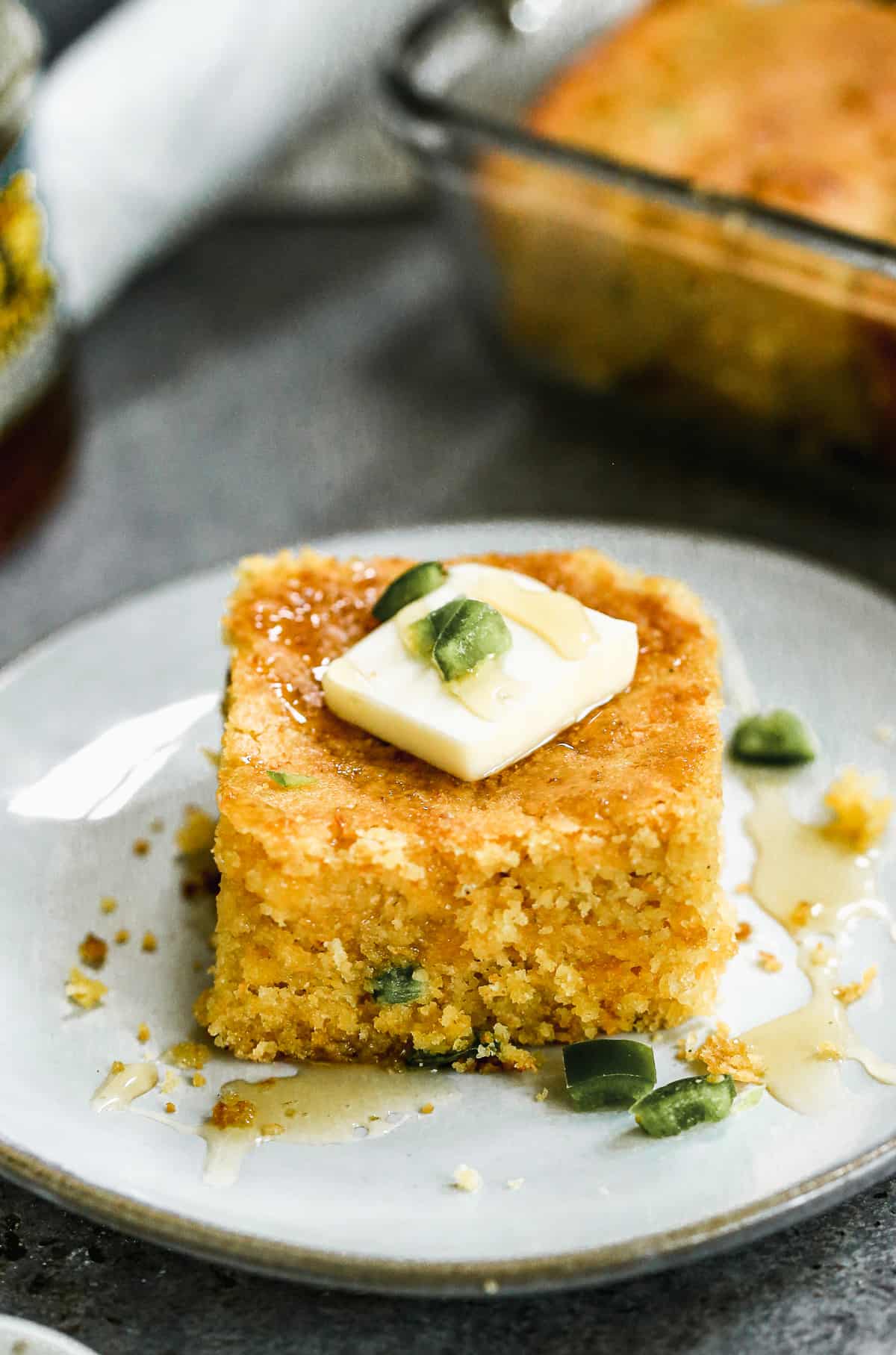 A plate with Jalapeño Cornbread with a square of butter and a drizzle of honey on top.