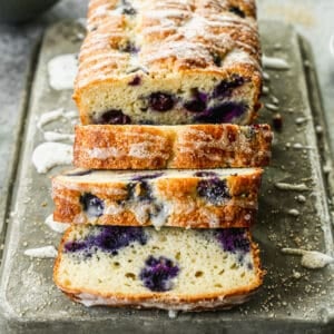 A loaf of Lemon Blueberry Bread with half of it sliced and ready to eat.