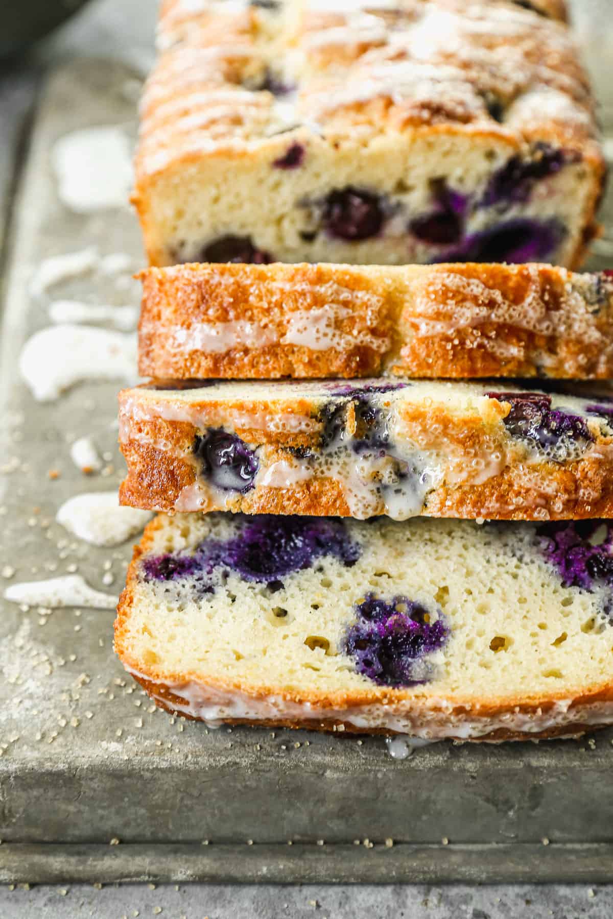 A close-up image of a sliced Lemon Blueberry loaf with a glaze drizzled on top.