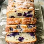 A loaf of the best Lemon Blueberry Bread recipe drizzled with a glaze and half of it sliced.