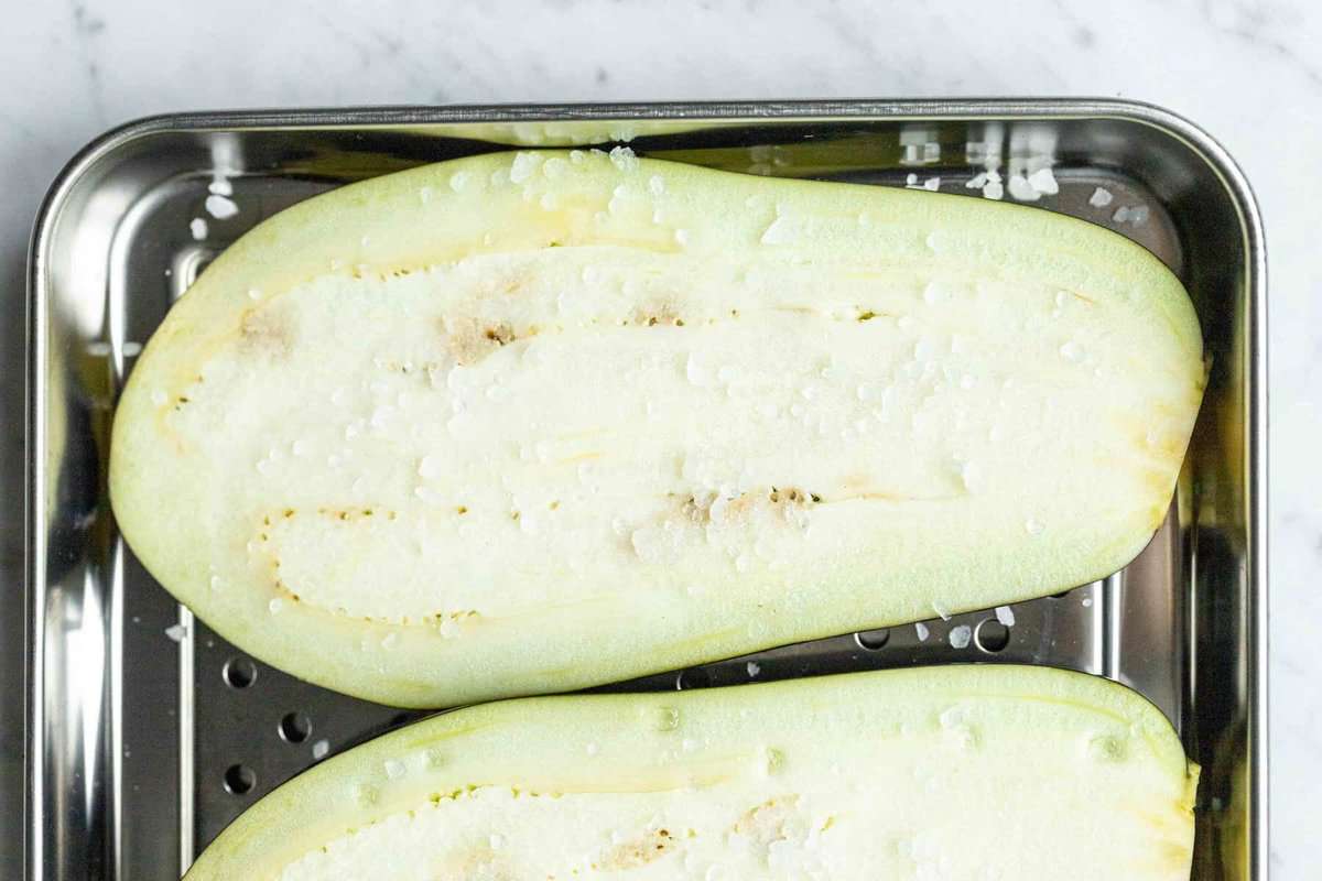 Sliced eggplant sprinkled with salt in a metal dish to release moisture for  the best Pasta Alla Norma recipe.