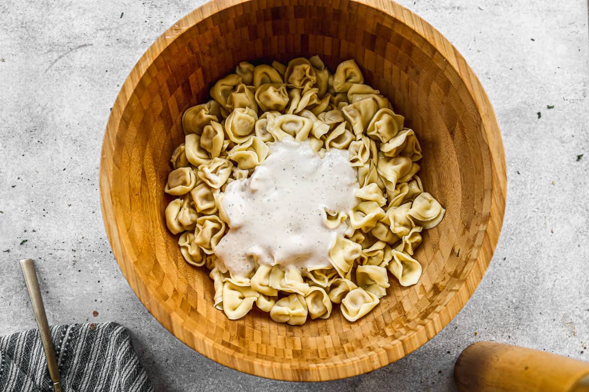 Cooked tortellini pasta with caesar dressing poured on top for the best Creamy Pesto Tortellini recipe.
