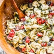 A wooden bowl filled with Pesto Tortellini salad, ready to serve.